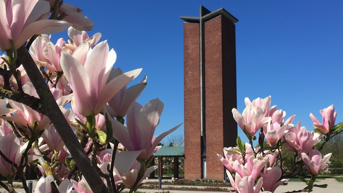 En høj murstenstårn med skråt tak og blomster i forgrunden