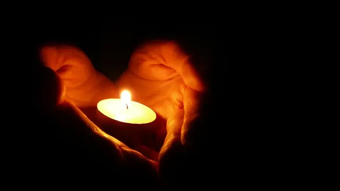 Hænder danner en hjerteform omkring et tændt lys.