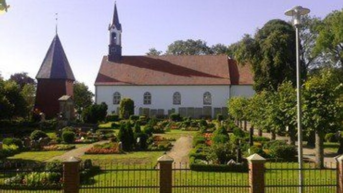 Weiße Kirche mit hohem Turm und rotem Dach in gepflegtem Garten.