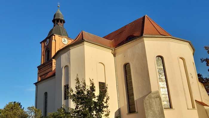 Kirchengebäude mit Uhrturm und rotem Dach unter blauem Himmel