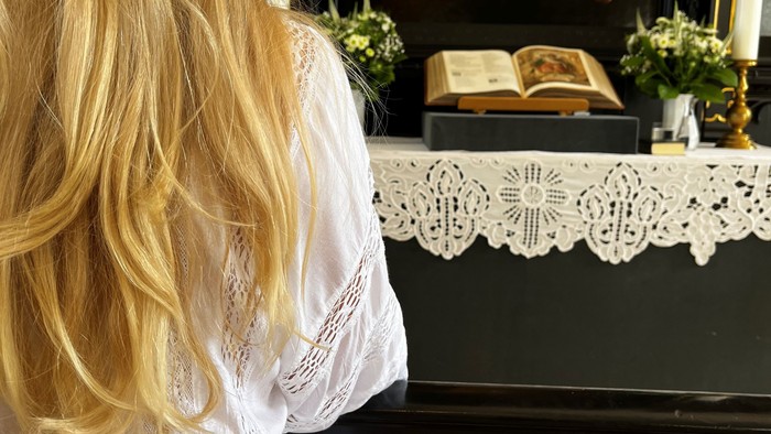 En kvinde med blond hår ser i et spejl med maleri og blomster.