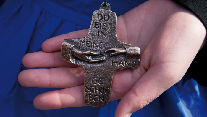 Hand hält ein kreuzförmiges Anhänger mit deutschem Text
