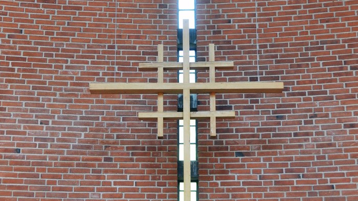 En stor korsformig lyskæde hænger på en mur af røde mursten.