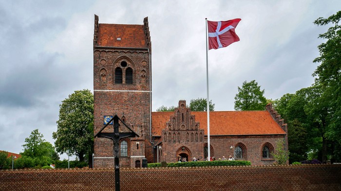 En rød murstenskirke med tårn og en dansk flag på en kæmpepæl.