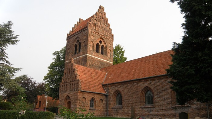 En gammel kirke med teglmur og tårn i en parkagtig omgivelse