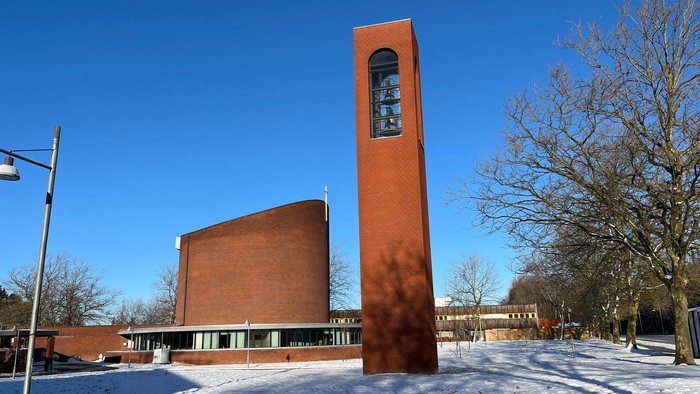 En rød murstenskirke med klokketårn og snedækket jorden foran