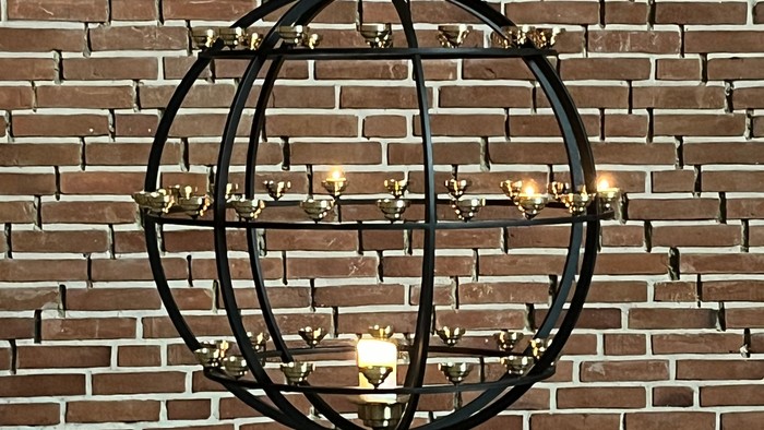 Elegant sort metal lysekrone med flere stearinlys-stil pærer sat op mod en murstensvæg.