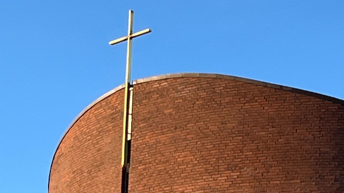 En stor mørk murstenskirke med et guldæret kors på toppen.
