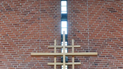 En stor korsformig lyskæde hænger på en mur af røde mursten.