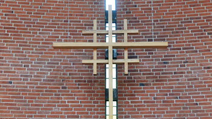 En stor korsformig lyskæde hænger på en mur af røde mursten.