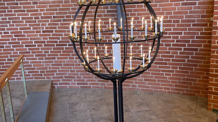 En stor kandelaber med mange lys på et podie foran mur af røde teglsten.