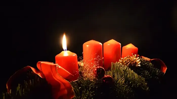 Drei brennende Kerzen inmitten von Tannenzweigen und Weihnachtsdekorationen