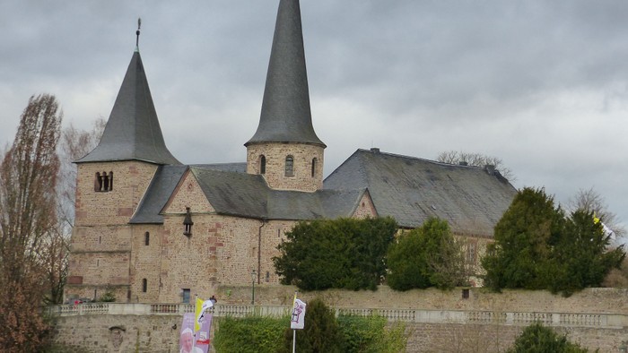 Historische Steinkirche mit Zwillingstürmen und Wehrmauern, vor bewölktem Himmel.