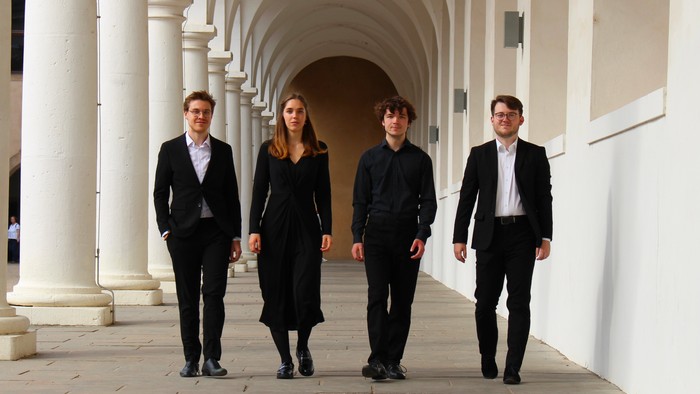 Vier Personen in formeller Kleidung gehen unter Arkaden
