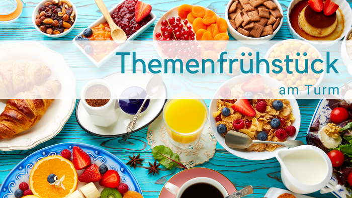 Hellblauer Holztisch mit Frühstückszutaten: O-Saft, Milchkännchen, obst, Cerealien, Tomaten, Croissant, Törtchen