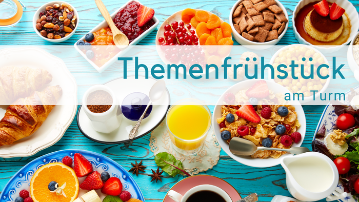 Hellblauer Holztisch mit Frühstückszutaten: O-Saft, Milchkännchen, obst, Cerealien, Tomaten, Croissant, Törtchen