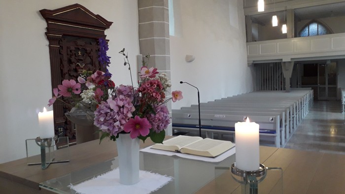 Kirchenaltar mit Blumen, Kerzen und einem aufgeschlagenen Buch
