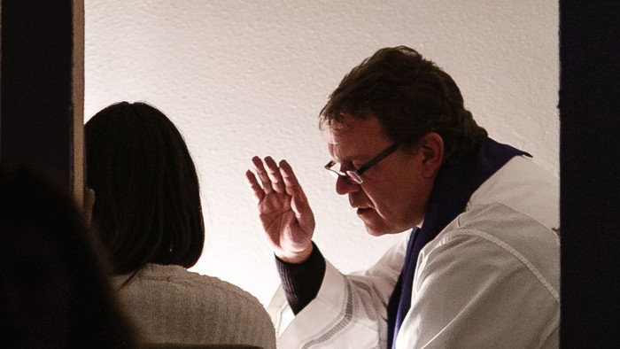 Ein Mann in weißem Anzug winkt auf einer Bühne.