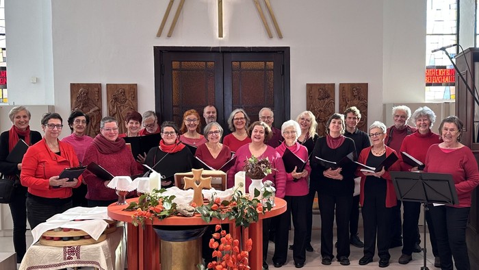 Eine Gruppe von Frauen in passenden roten Jacken, die während eines Gottesdienstes in einem Kirchenchor singen oder auftreten.