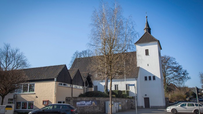 Ein weißer Kirchturm mit spitzem Dach neben einem Haus mit Autos davor