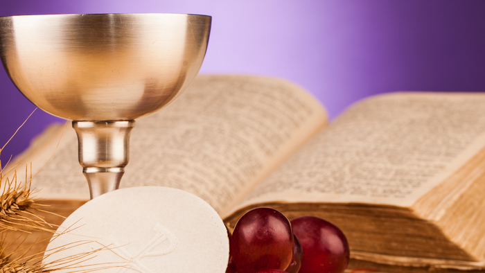 A chalice, bread, and grapes are placed near an open book