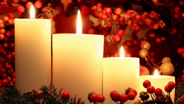 Three lit candles surrounded by berries and greenery.
