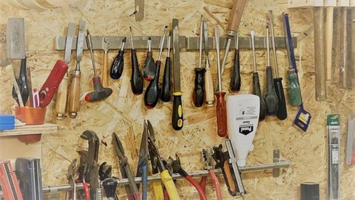 Verschiedene Werkzeuge, die an einer Holzwand hängen, darunter Zangen, Schraubenschlüssel und Schraubendreher.