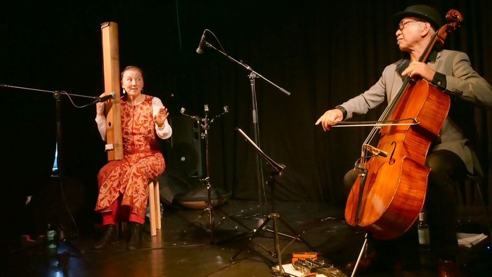Zwei Musiker treten auf der Bühne auf, einer spielt Cello, der andere ein Blasinstrument.
