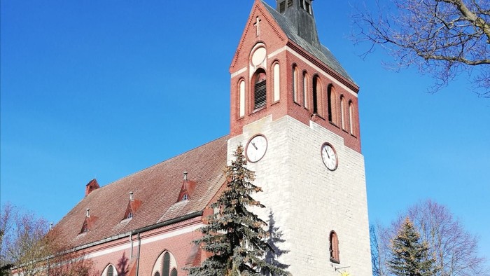 Kirchturm mit Uhr und spitzem Dach vor blauem Himmel