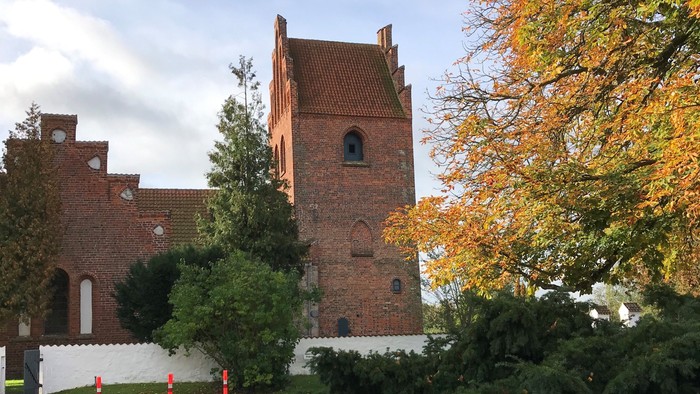 Et rødt teglmurstenshus med tårn og træer i forgrunden