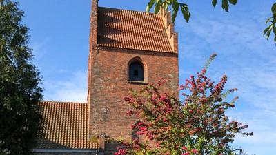 En gammel kirke med tårn og murvej ved en grøn plads
