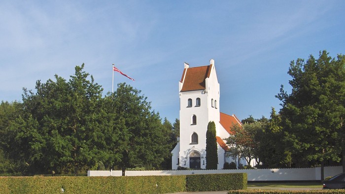 En hvid kirke med rødt tag og en flagstang med flag ved siden af.
