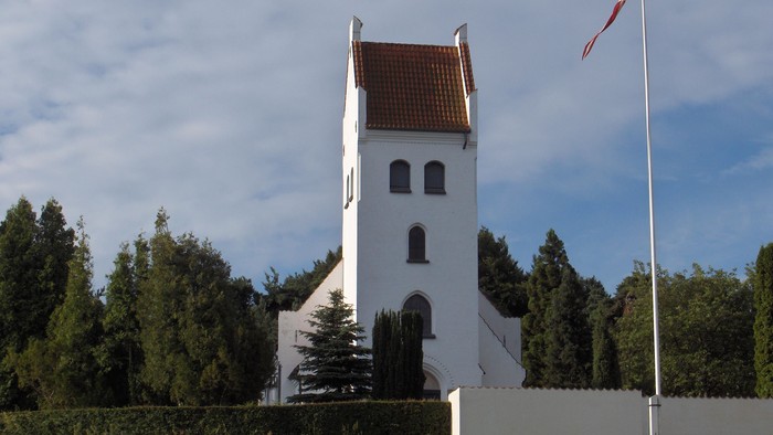 En hvid kirke med klokketårn og en flagstang med flag.