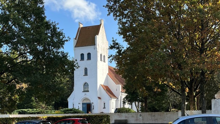 En parkering med tre biler foran et hvidt hus med røde tag.