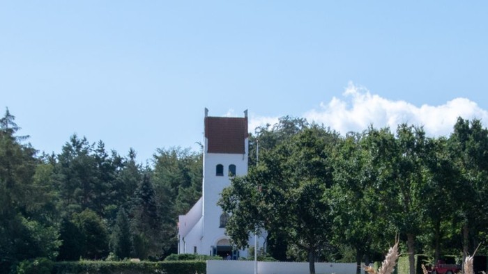 En høstmark i forgrunden med et hvidt tårn og træer i baggrunden