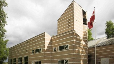 Bygningen har en moderne og geometrisk design med horisontale linjer og en flagpole med rødt flag.