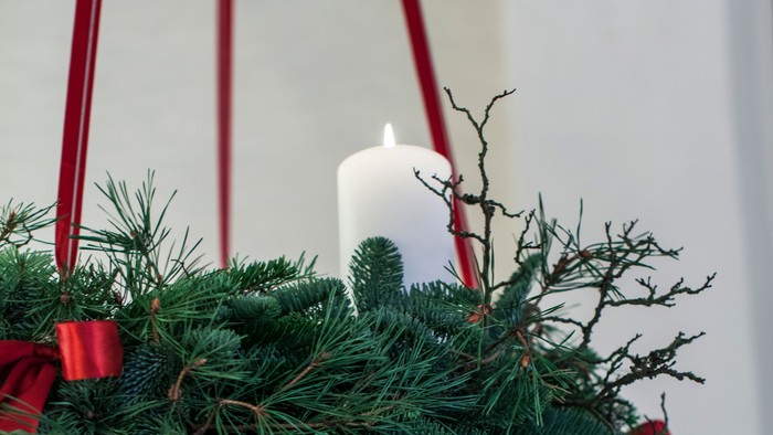 En hængende julekrans med lys og røde bælter.