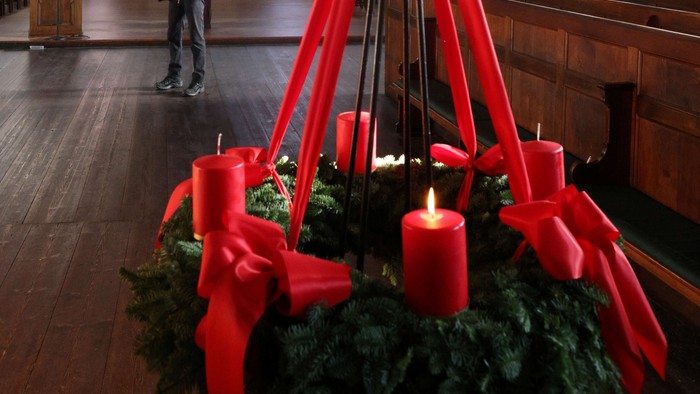 In der Kirche steht ein Adventskranz mit vier Kerzen und roten Schleifen.
