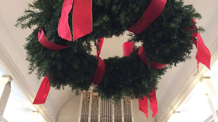 Ein großer Weihnachtskranz mit roten Schleifen hängt an der Decke.