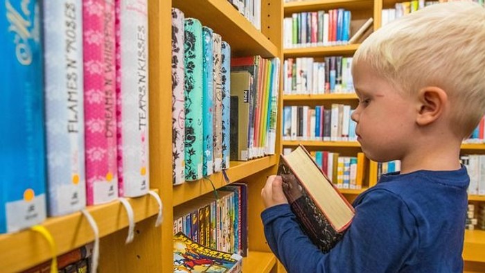 Ein kleiner Junge steht in einer Bibliothek und schaut sich Bücher an.