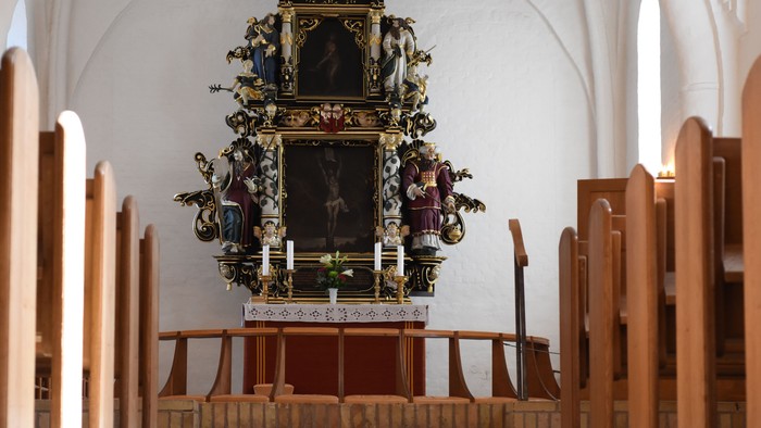 Indre del af kirke med altertavle og bænke.