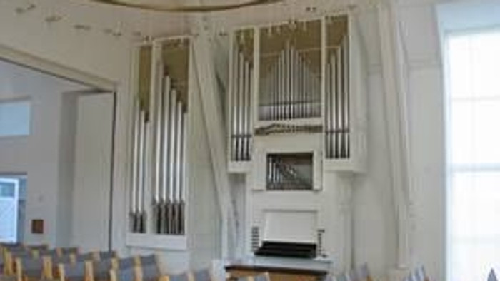 En stor kirke med hvidt orgel og træstoler.