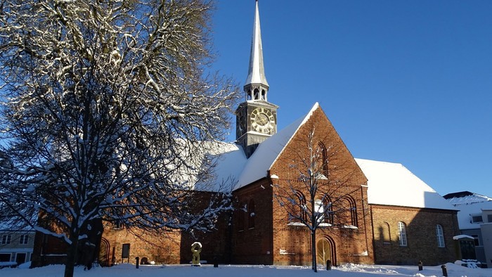 En snede kirke med klokketårn og en især snebelagt træ foran