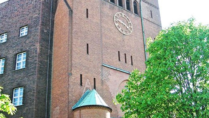 Grosses Ziegelgebäude mit Uhrturm und grünen Bäumen davor