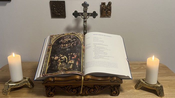 Ein offenes Buch mit Kreuz und Kerzen auf einem Tisch