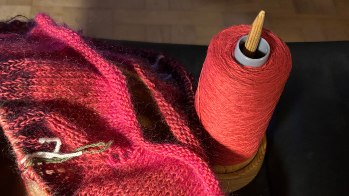 En håndklædet i røde og brune farver ligger på bordet ved siden af en spole med rød tråd.