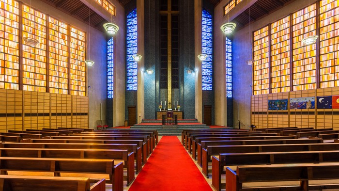 Die Kirche mit roten Teppich und Holzbänken, große Fenster mit Licht.