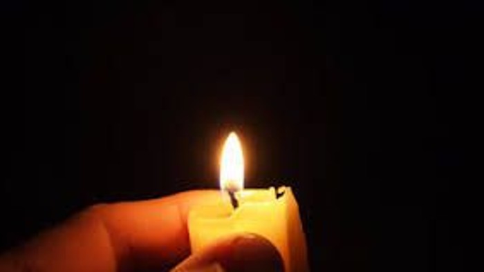 En hånd holder en lystende lyse stearinlys i mørke omgivelser.