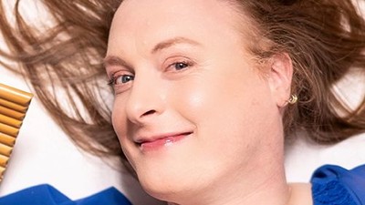 Eine fröhliche Person mit wilden Haaren und einem blauen Oberteil, die sanft lächelt, während sie eine Haarbürste hält.