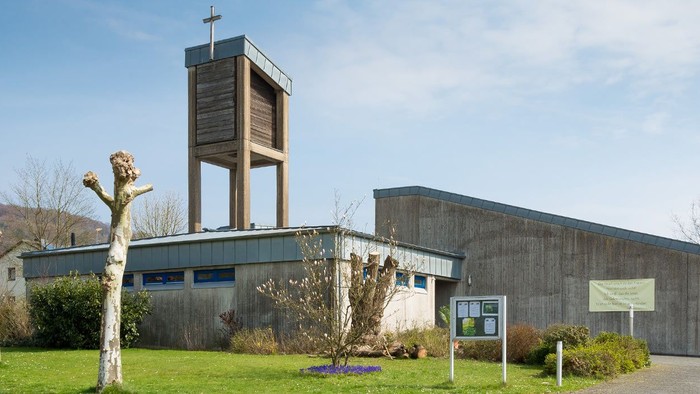 Moderne Kirche mit hohem Kreuz und Skulptur davor.